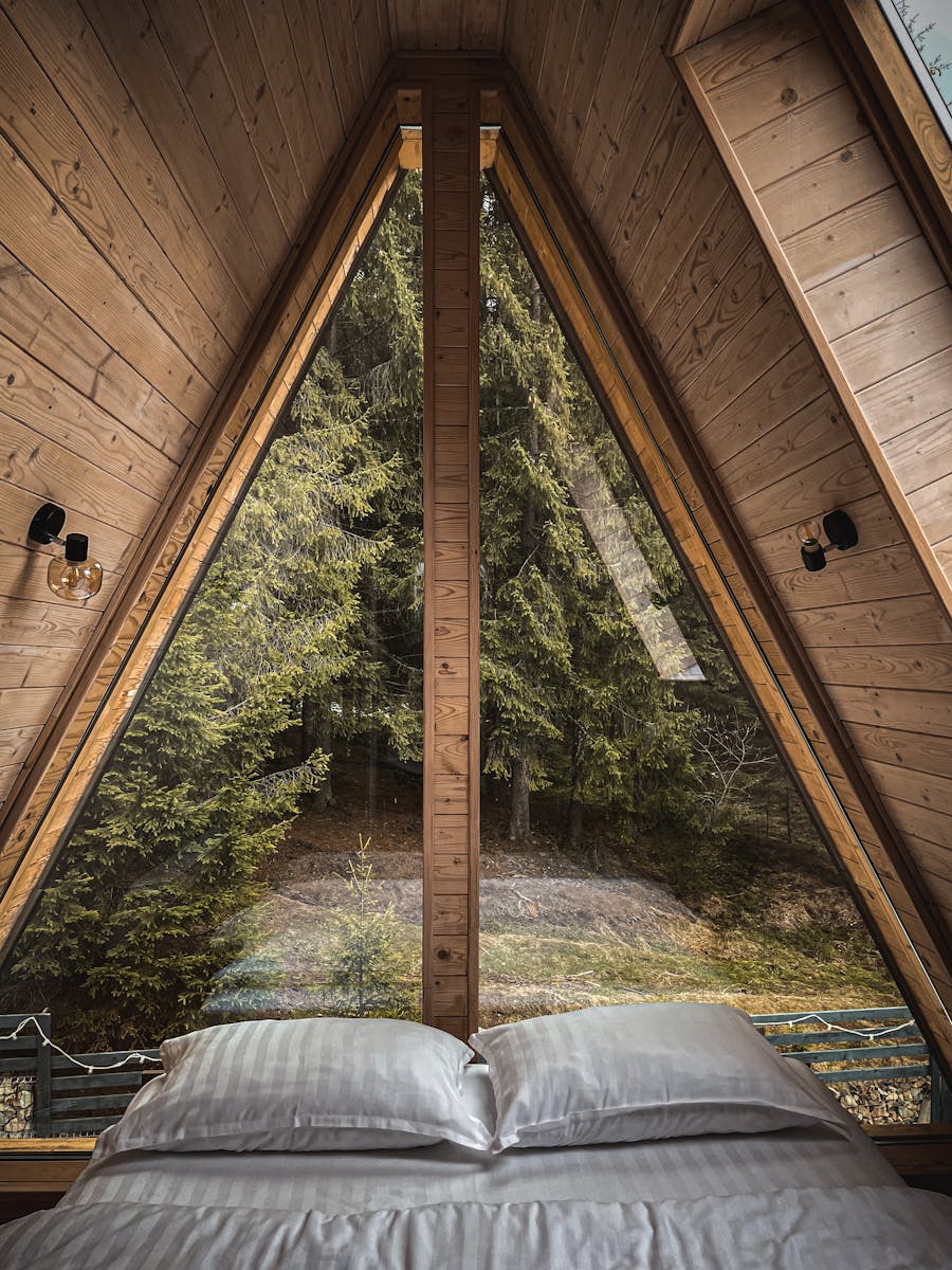 A serene A-frame cabin bedroom with forest view through large triangular windows.