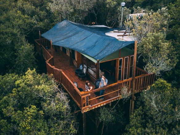 Aerial view of a rustic treehouse cabin surrounded by lush forest in South Cape DC, South Africa.