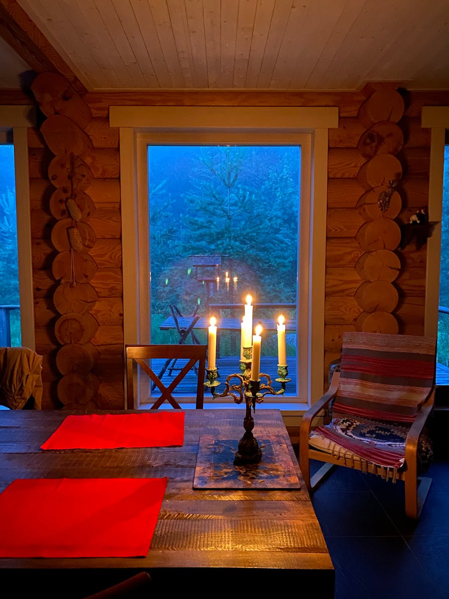 Warm candlelight on a wooden table in a rustic cabin interior with forest view.